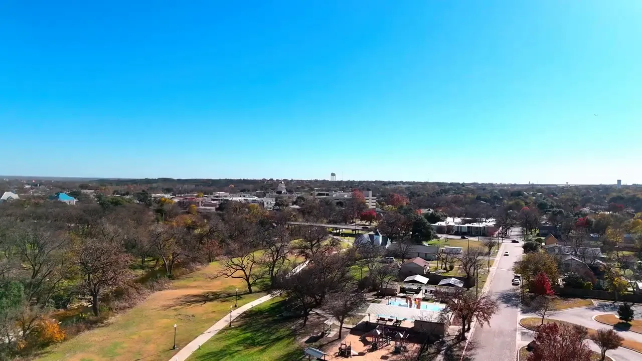 Panoramic aerial view of a small town with park, trees, houses and downtown buildings under a bright blue sky