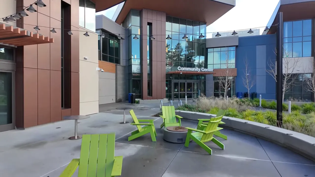 Host standing on a lagoon promenade beside a green construction fence with a sign about the new recreation center.