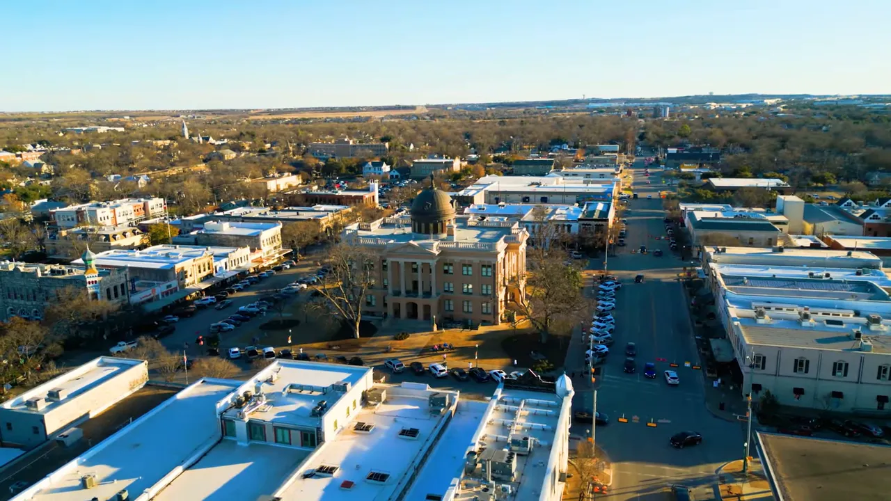 Presenter at a park fence with open field and rolling hills in the background, capturing suburban landscape context.
