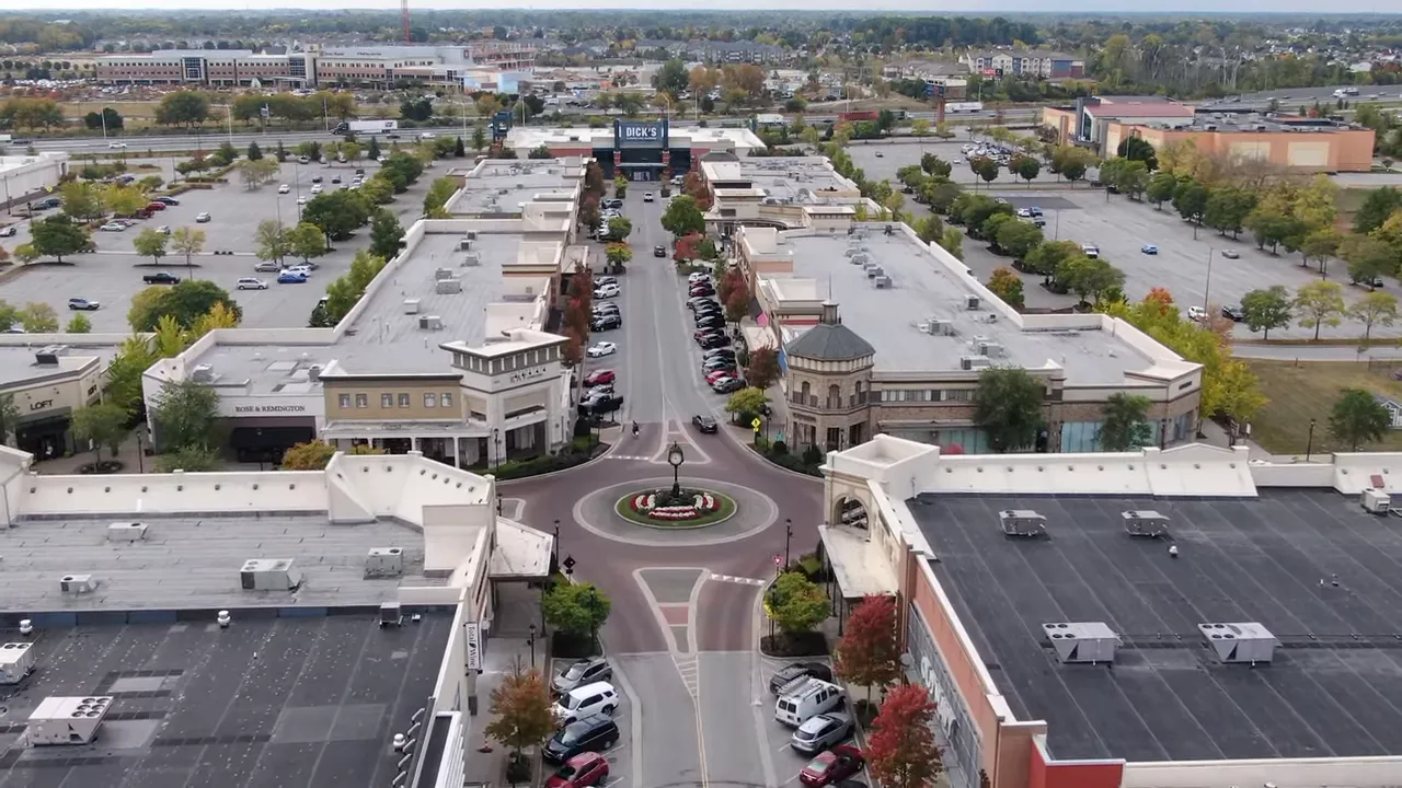 Aerial shot of a large shopping corridor and roundabout with parked cars, illustrating suburban retail scale.