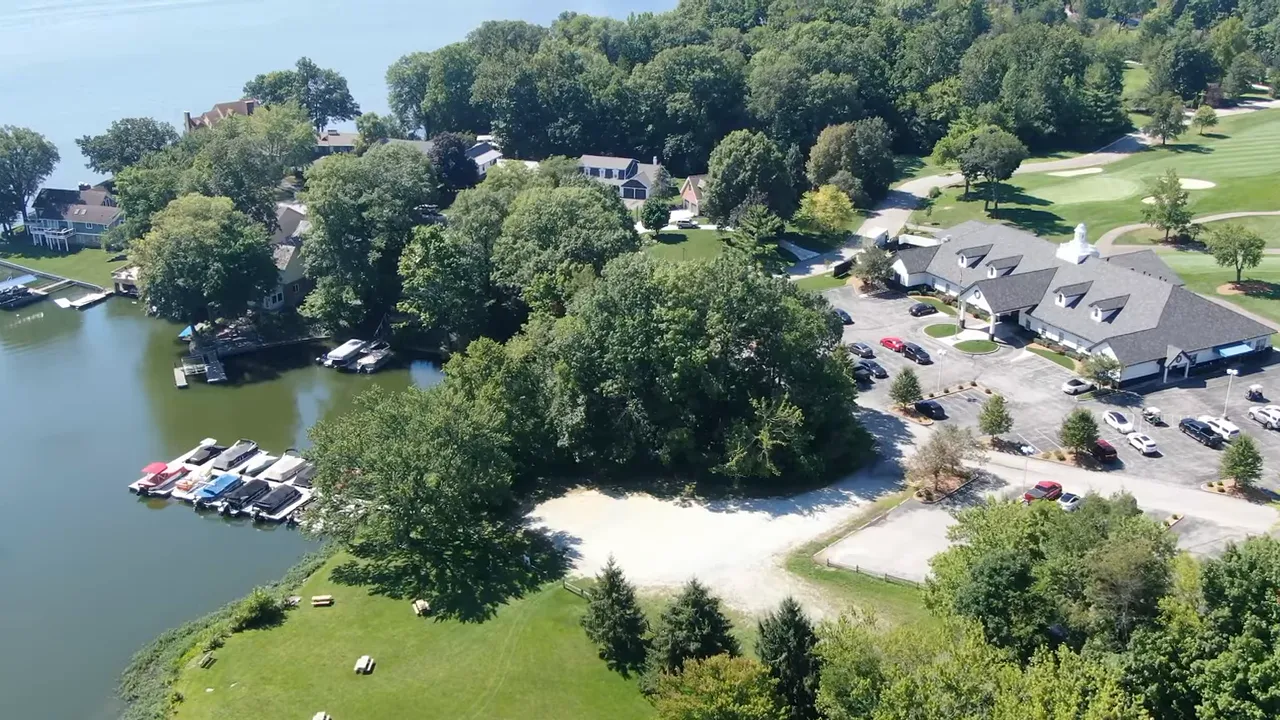 High-angle drone view of a suburban neighborhood with houses, ponds, roads and tree lines.