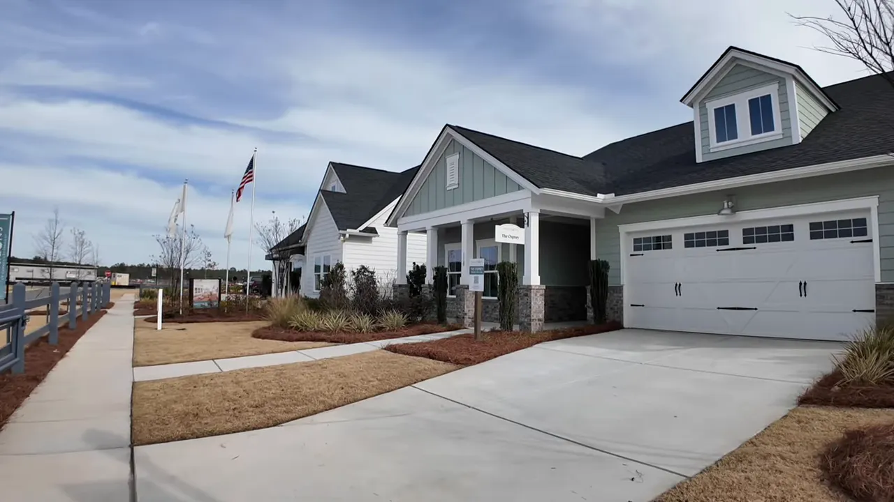 Front exterior of the Osprey model home with light-blue hardy plank siding, brick knee wall, landscaped yard, driveway, and two-car garage.
