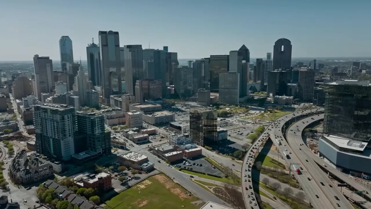 Heavy traffic fills a Dallas freeway with downtown buildings in the background
