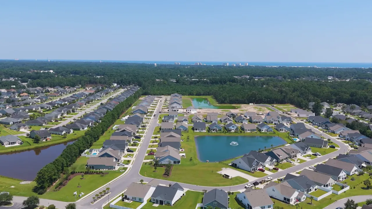 Aerial neighborhood view with pond, homes and the ocean on the horizon showing proximity to the beach