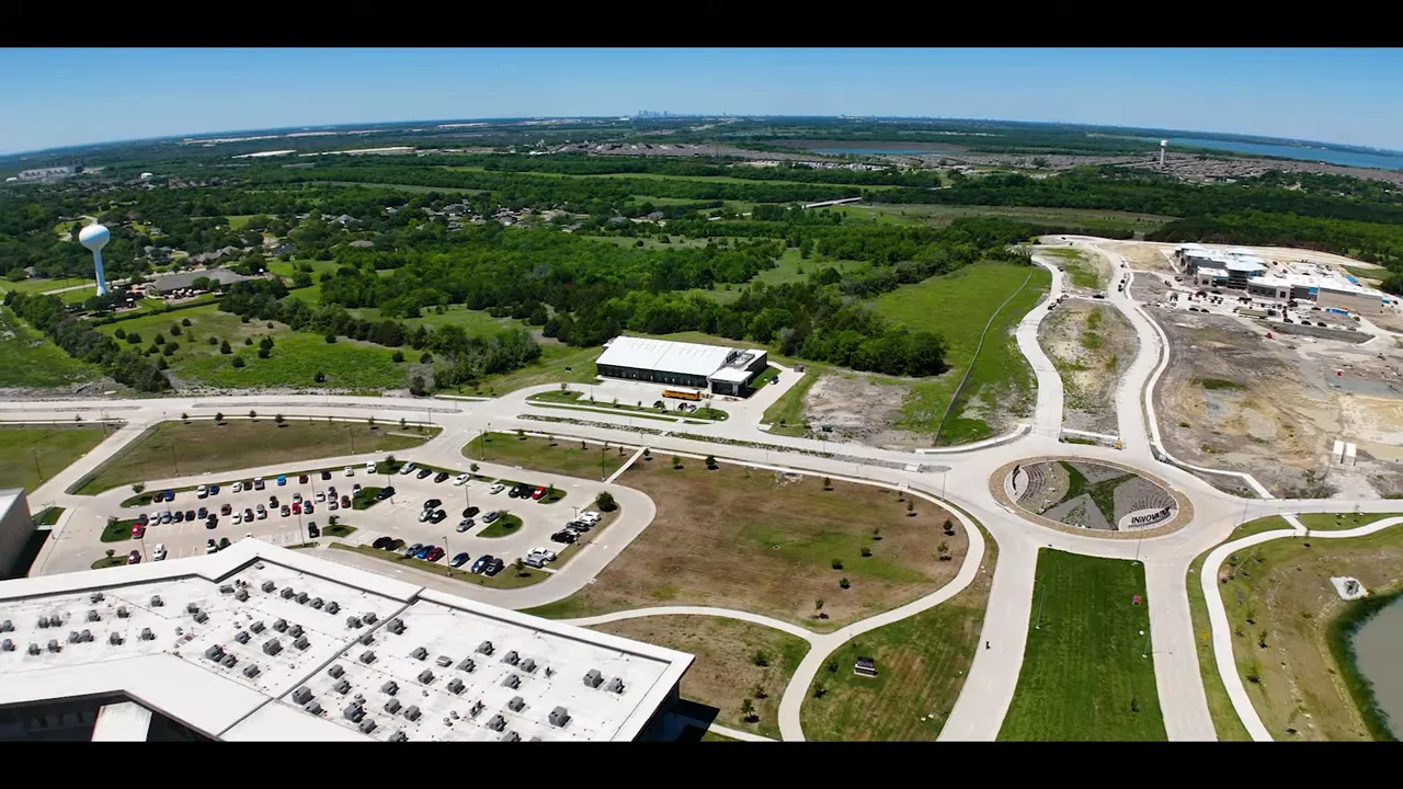 Wide shot of two hosts seated at a table with a large screen displaying a map of Forney and nearby areas; microphones and laptop visible.