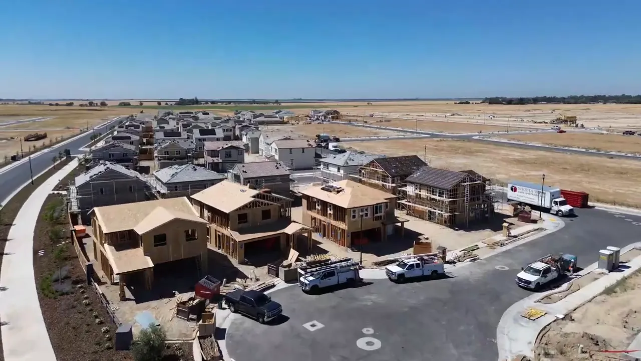 Podcast host speaking and gesturing with hands while co-host listens, microphones and laptop visible, blue backlight