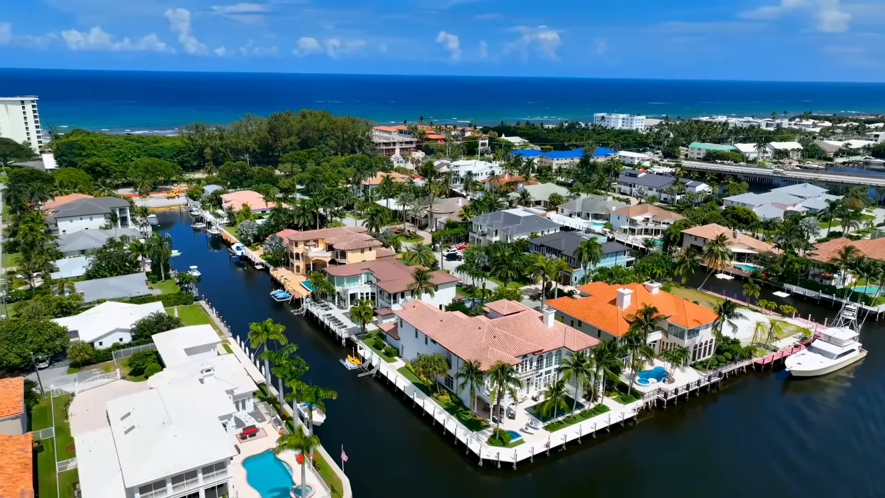 Gated estate driveway flanked by large palm trees with a white entry gate and mansion beyond, showing a luxury Delray Beach property.
