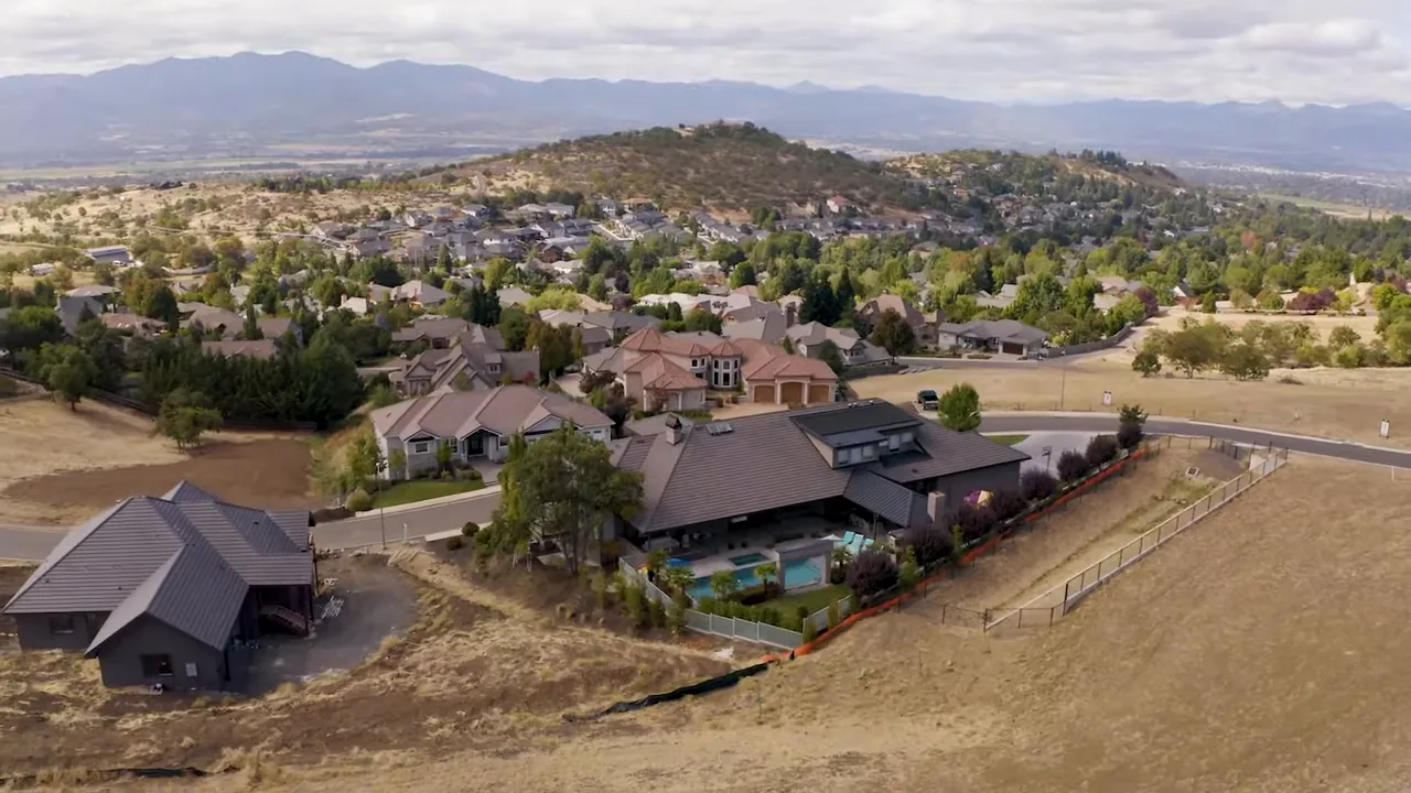 Presenter standing in a grassy park with houses and trees in the background, illustrating Southern Oregon neighborhood and open space.
