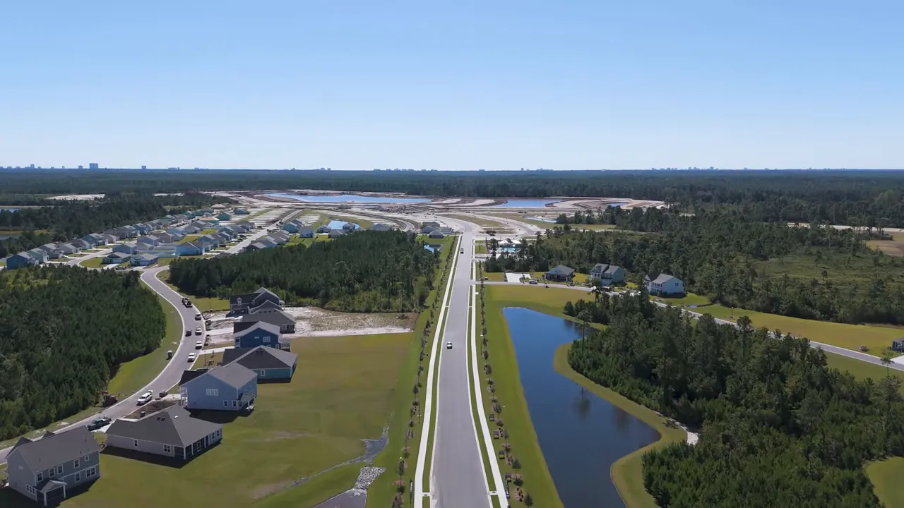 Aerial drone view of a new residential subdivision with road, ponds, and houses under construction