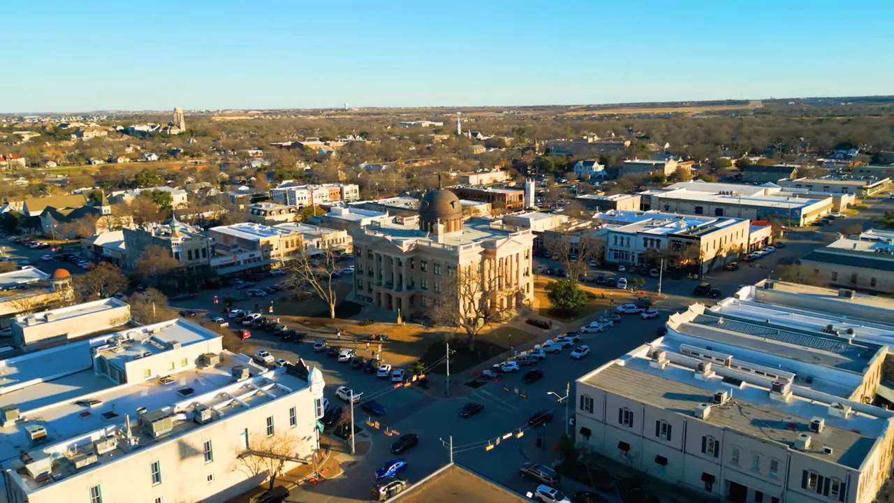 Presenter at a downtown intersection with a visible water tower and street sign in the background