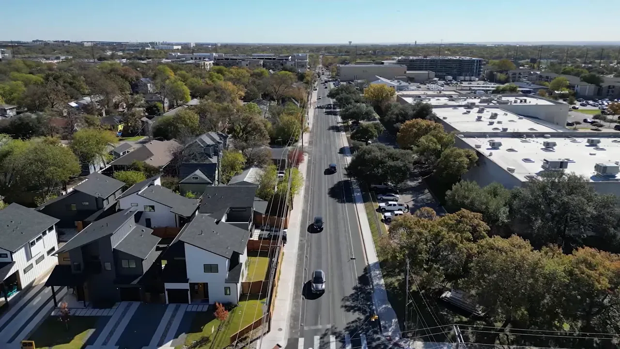 Front exterior of an older bungalow with the presenter pointing toward the house, showing the driveway, lawn and mature trees.