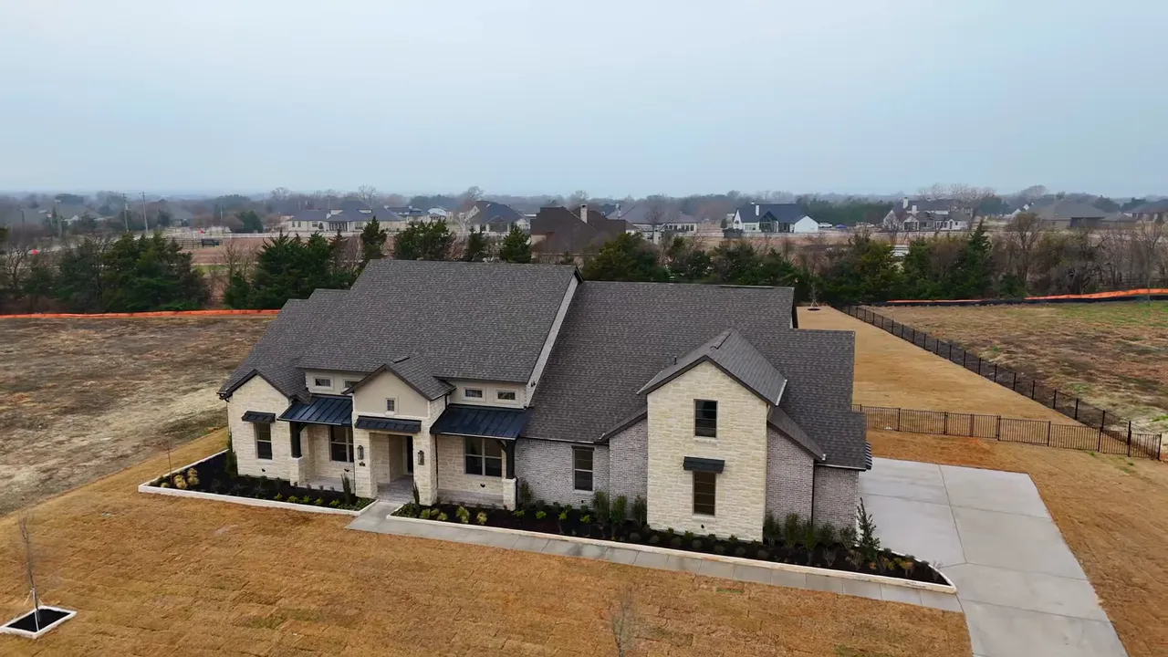 Front exterior of a two-story stone home showing detailed stonework, garage doors and wide driveway with presenter inset