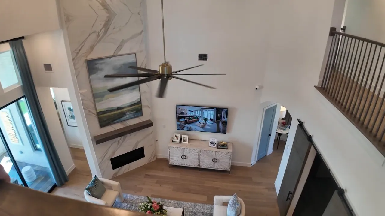 View from upstairs railing into family room with tall ceiling and large fan