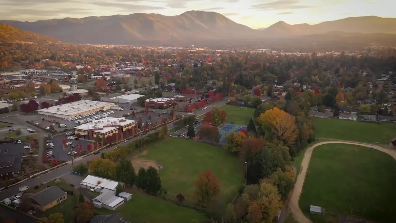 Presenter in a studio with a 'Buying Southern Oregon' lightbox and large on-screen text that reads 'COME & VISIT'.
