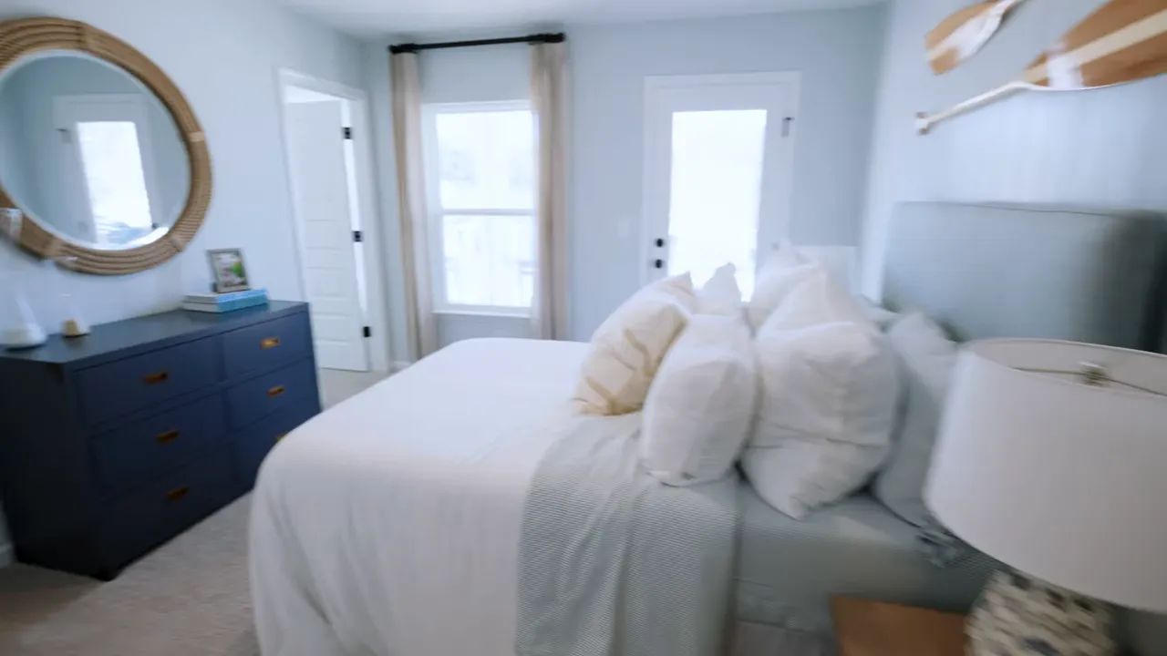 Upstairs bedroom with a large window, dark dresser, arched mirror, and neutral carpeting in a North Myrtle Beach new construction home
