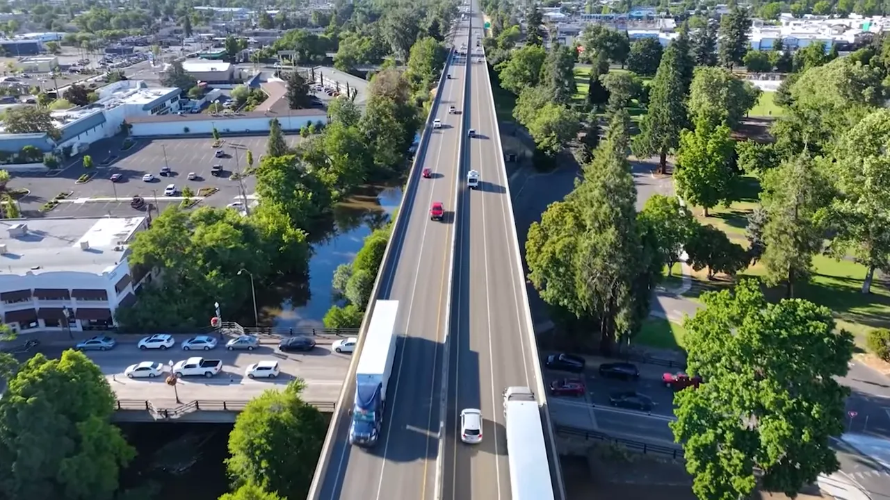 Presenter standing in Ashland East Main Community Park with fall foliage and an on-screen '2,000 residents' graphic