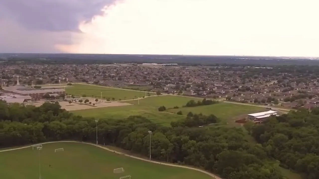 Split-screen screenshot showing the interior of a vehicle on the left and a curved newly paved road with sidewalks and bare lots on the right in the Meraki development.