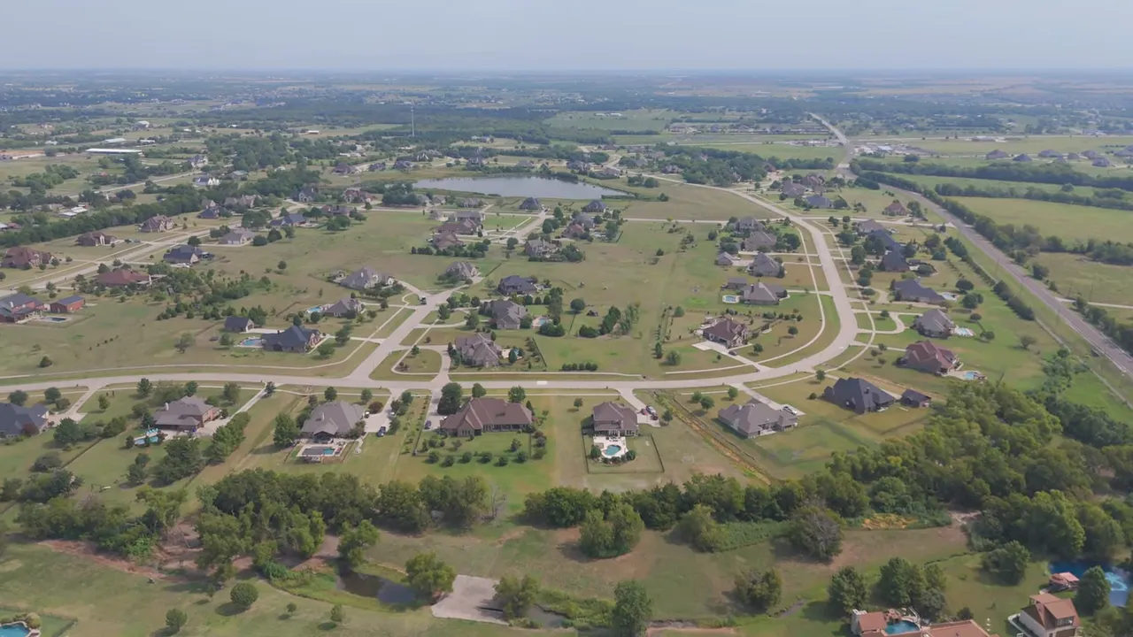 Wide front exterior of a large modern farmhouse estate with gabled wings, central glazed entry and illuminated windows at sunset.