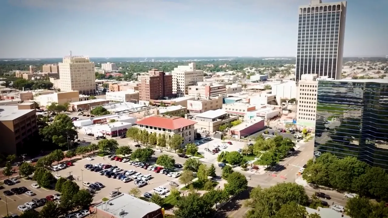 Host mid-gesture in a home studio with guitars, percussion and a yellow couch in the background, discussing community character