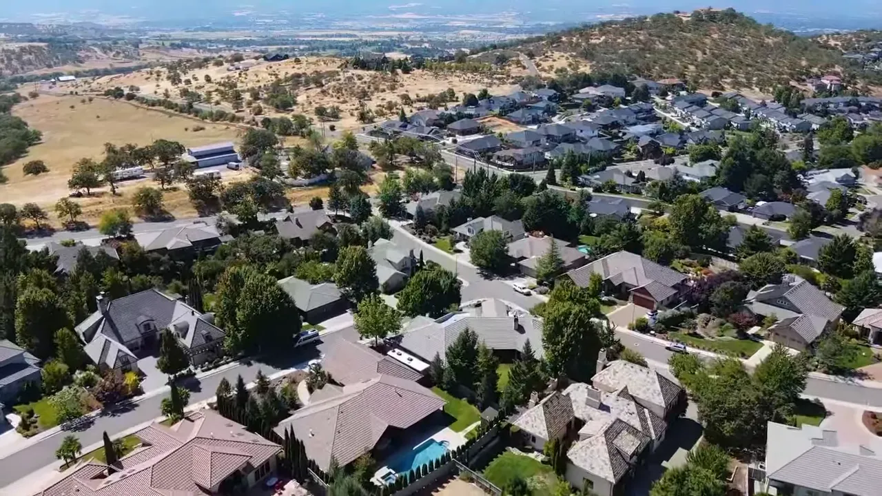Interview still in an office showing a host with a lower-third card reading 'What is the cost of living in Southern Oregon?'