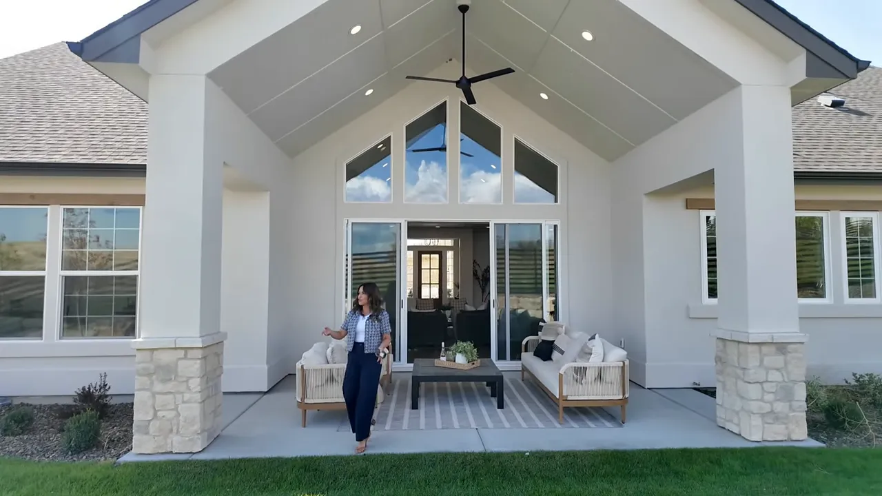 Covered patio seating area with coffee table and green backyard lawn backed by a rock retaining wall and horizontal fence