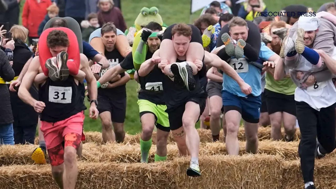 Mehrere Männer tragen ihre Partnerinnen über Strohballen bei einem Ehefrau-Trage-Rennen, Hindernislauf-Szene