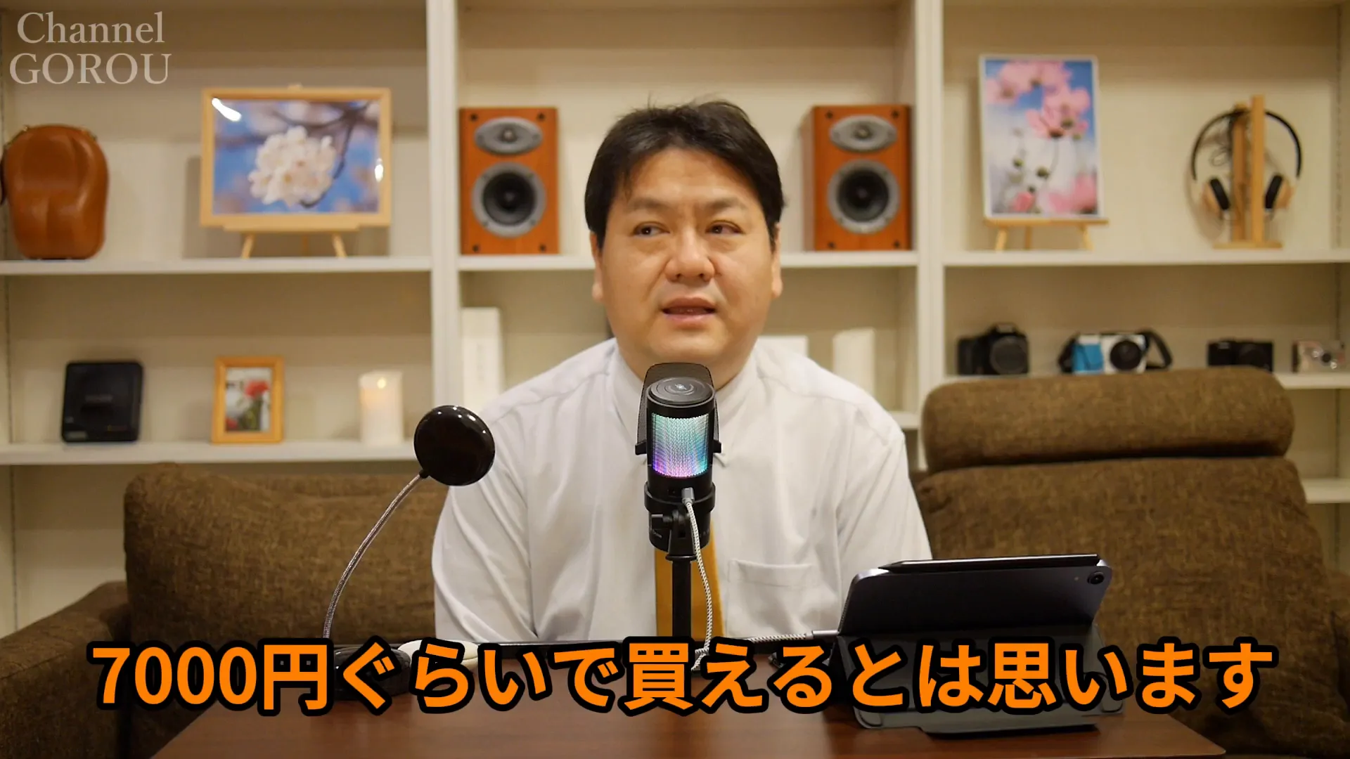 テーブル中央のマイクとレビュワー、画面下に『7000円ぐらいで買えるとは思います』の字幕が表示されたスクリーンショット。
