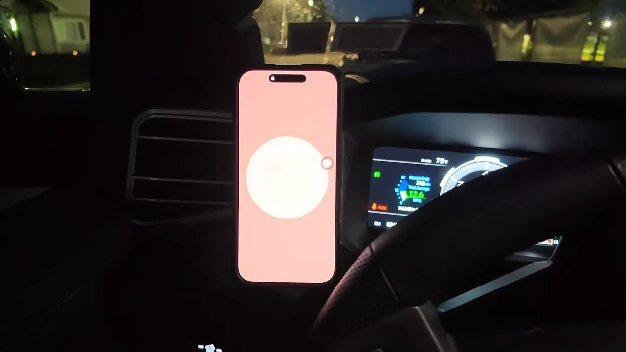 Phone attached vertically to a glowing circular magnetic charger beside the steering wheel at night