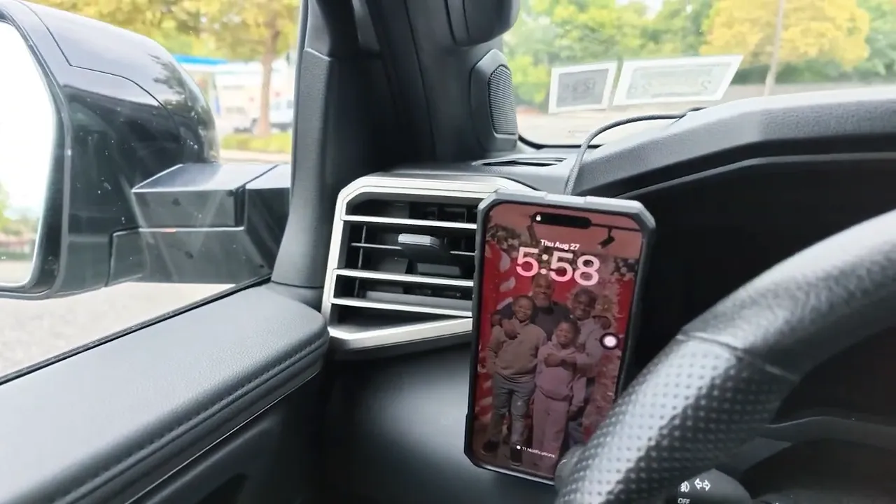 Phone mounted vertically on a circular charger beside the driver-side air vent and steering wheel
