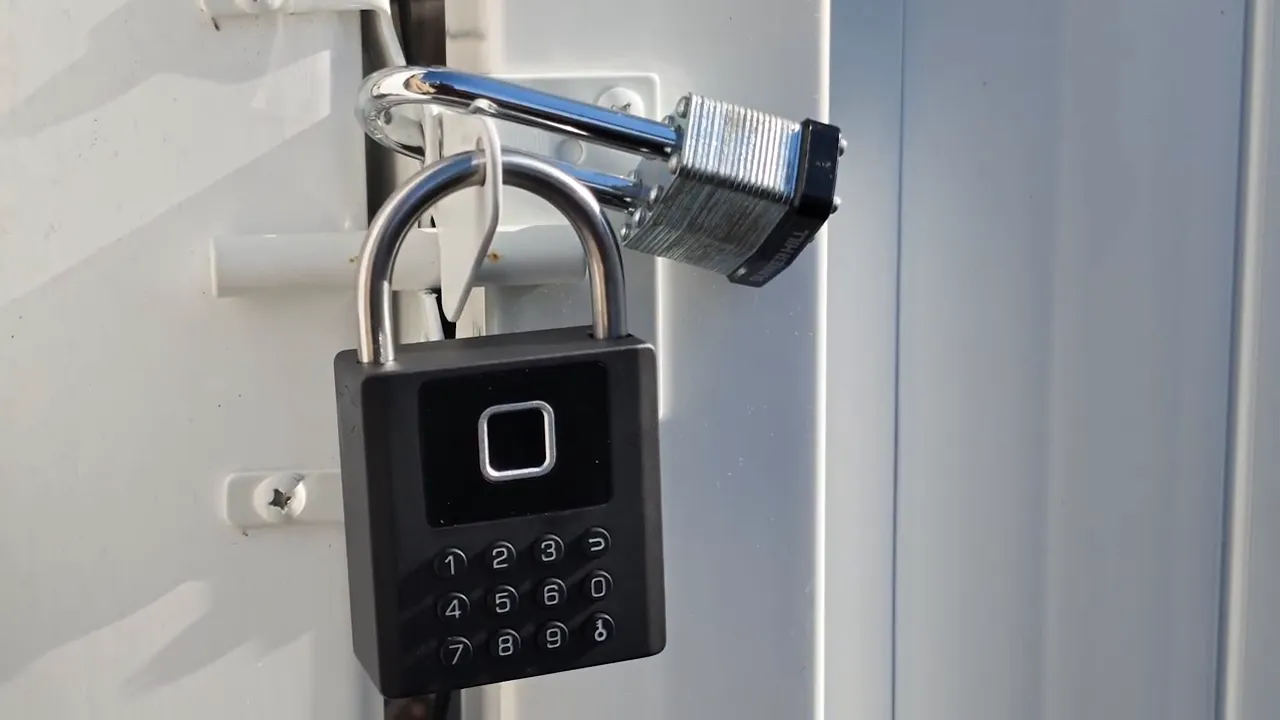 Black smart padlock hanging from a white outdoor gate latch