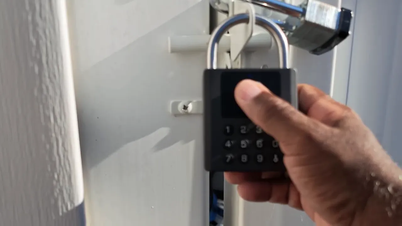 Hand pressing the fingerprint sensor on a black smart padlock mounted on a gate