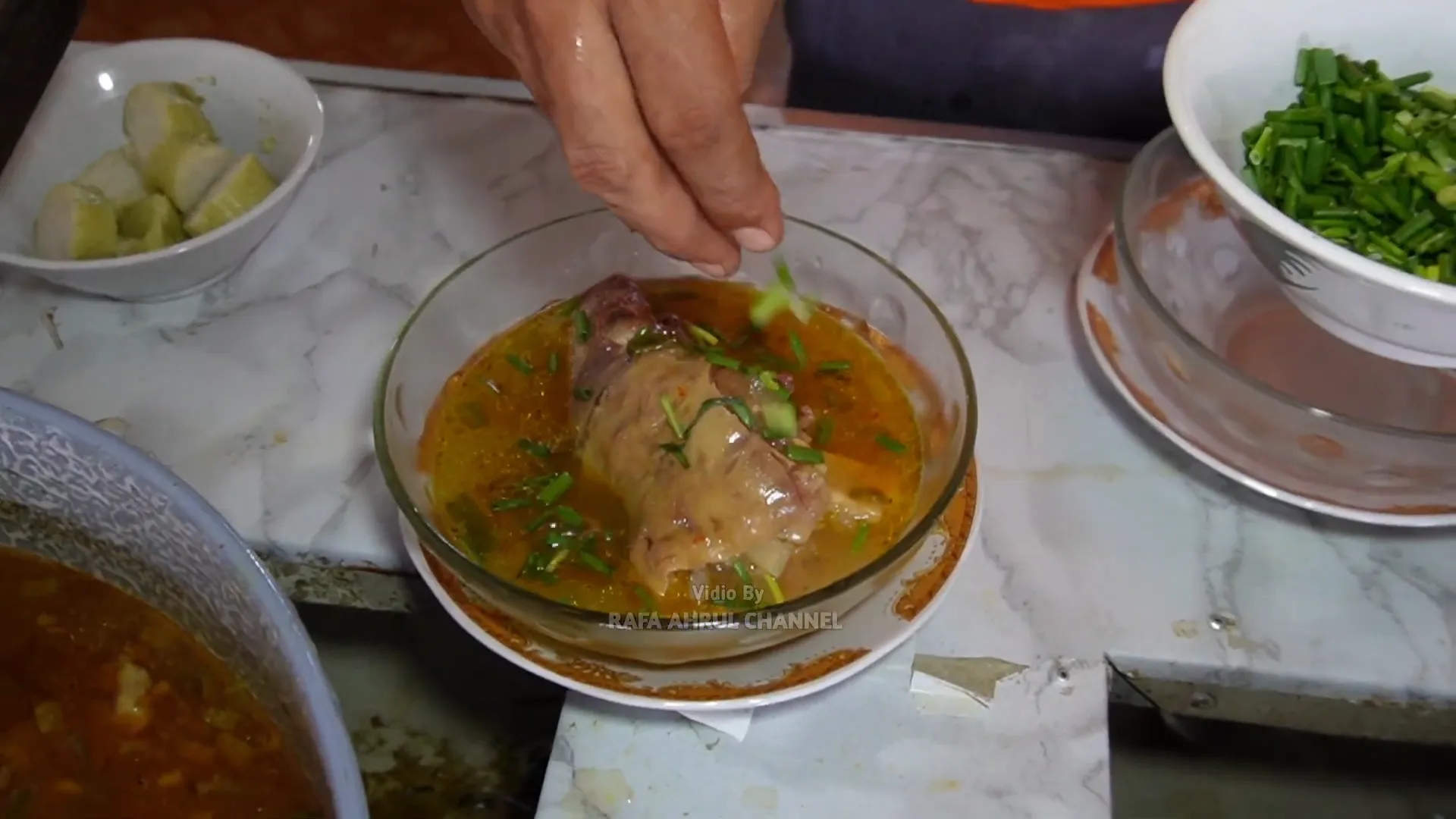 Taburan bawang goreng dan daun bawang di atas lontong kikil