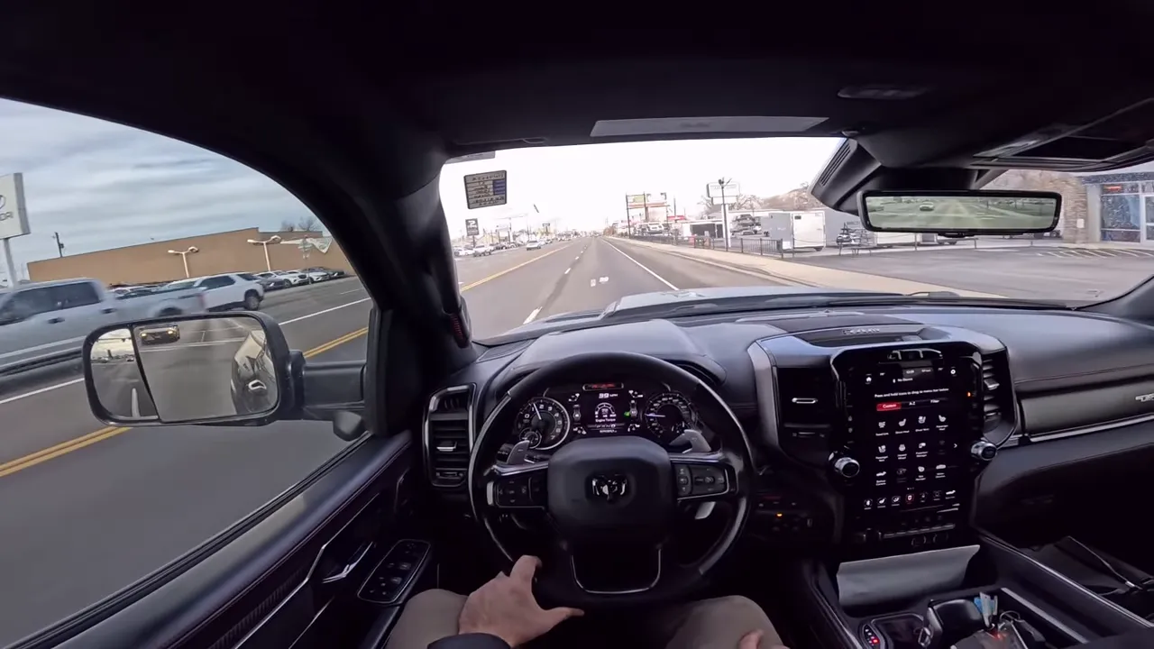 Centered driver POV of a Ram TRX showing steering wheel, instrument cluster, large infotainment screen and open road ahead