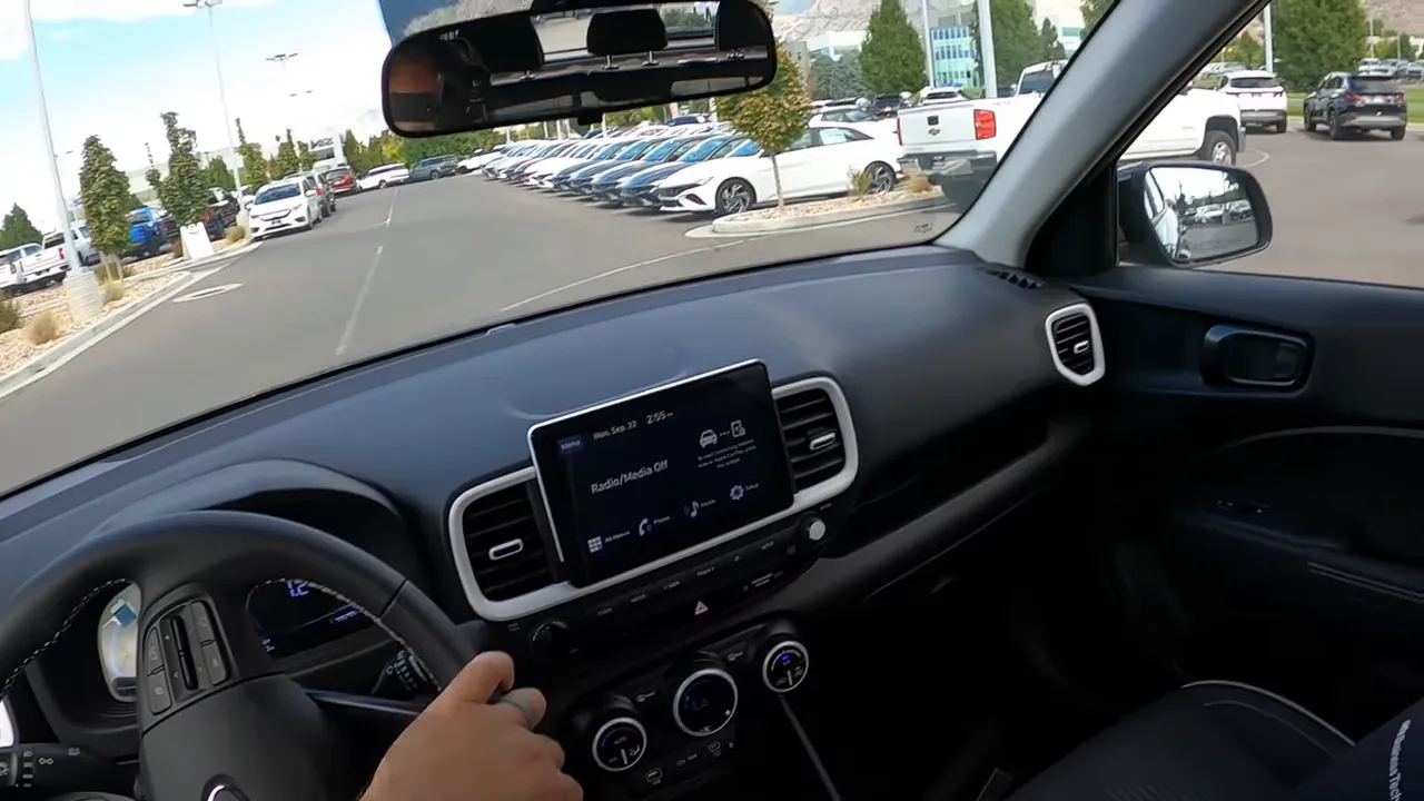 Driver's view over the dashboard toward a dealership lot lined with new cars