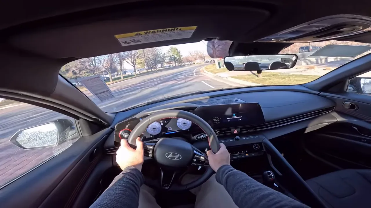 Wide driver view of the Hyundai Elantra N-Line showing both hands on the wheel, dashboard and a clear curve in the road ahead.