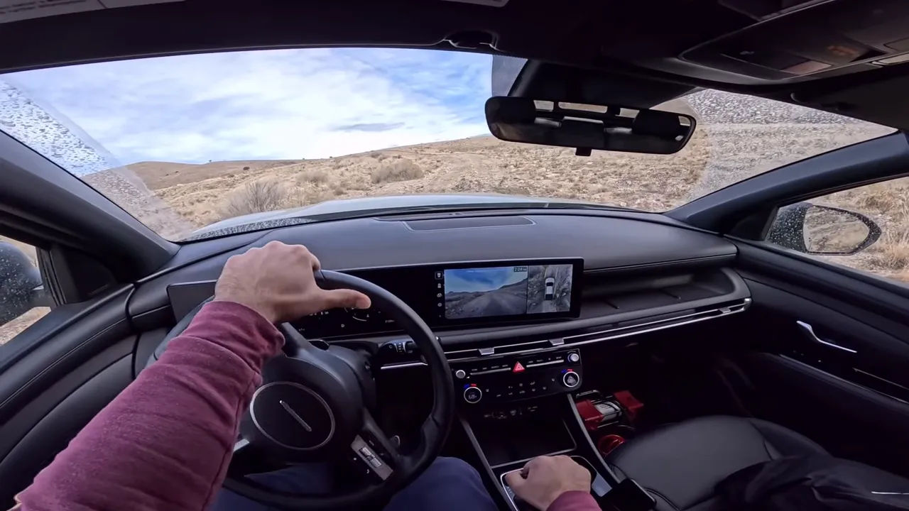 Driver perspective inside Santa Cruz showing center camera feed and rough trail while negotiating an obstacle