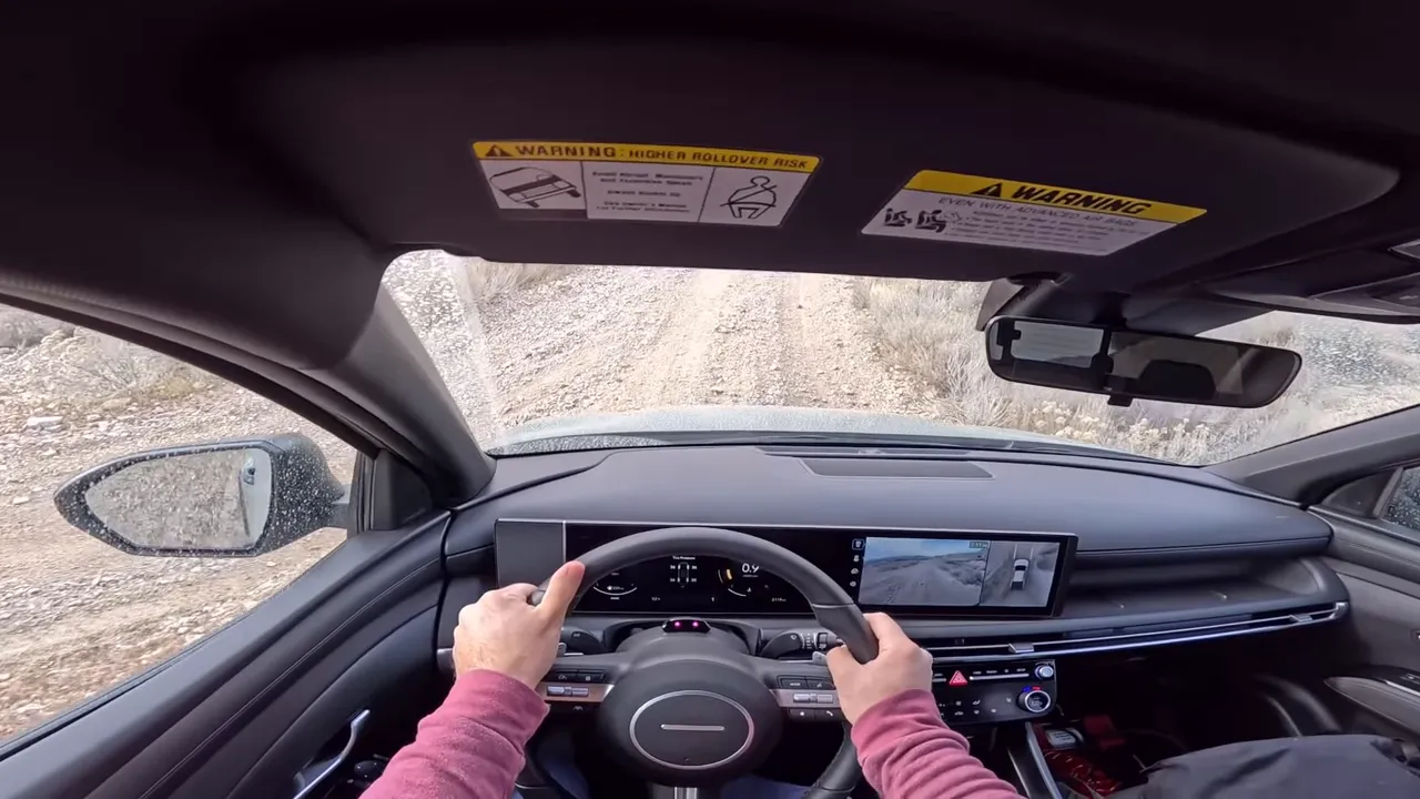 Driver POV with both hands on the wheel, dashboard visible and a steep rocky trail directly ahead in the Hyundai Santa Cruz XRT.