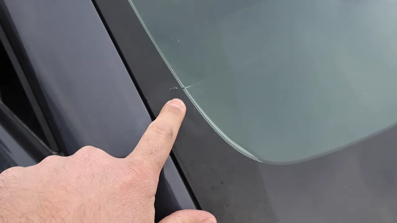 Close-up of fingertip pointing to a crack at the edge of a CX-50 windshield near the ceramic frit