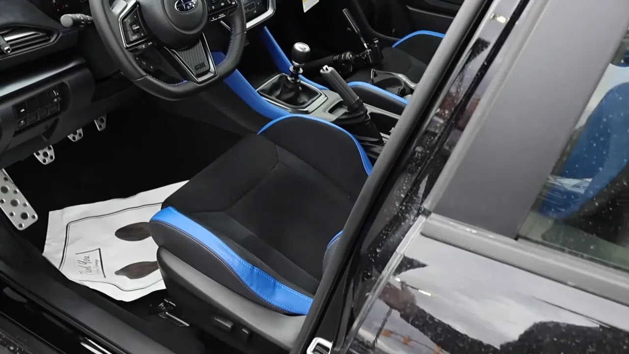 Front driver seat and cockpit of Subaru WRX TS showing blue trim, steering wheel and manual shifter