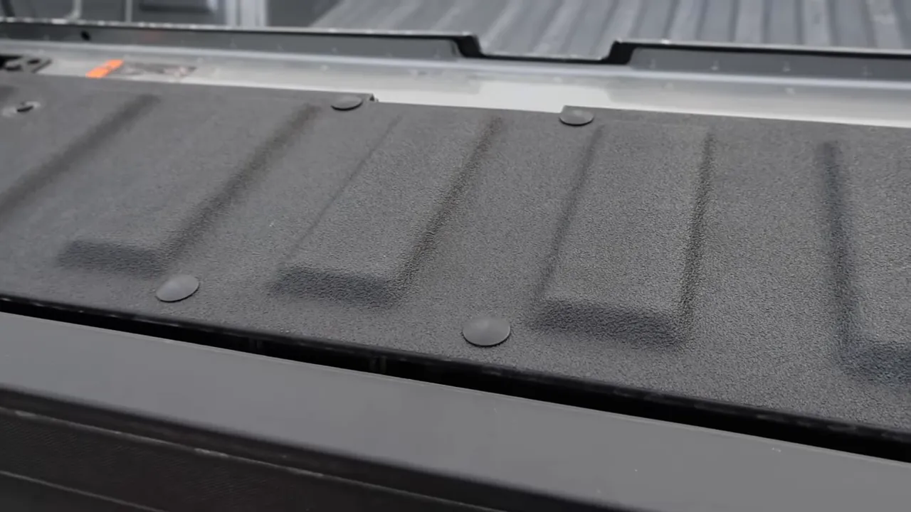 Close-up of truck tailgate edge showing textured bedliner and plug fasteners