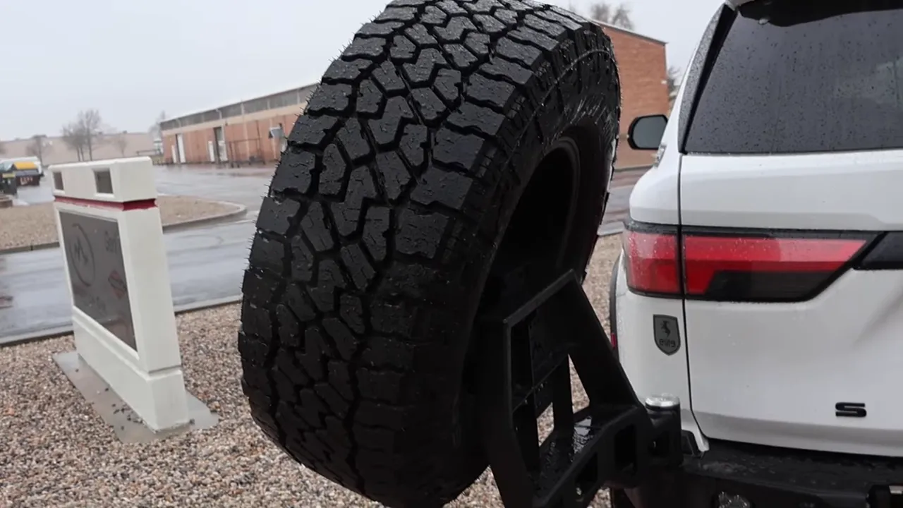 Large off‑road spare tire mounted on a swing‑out attached to the rear of a white Sequoia