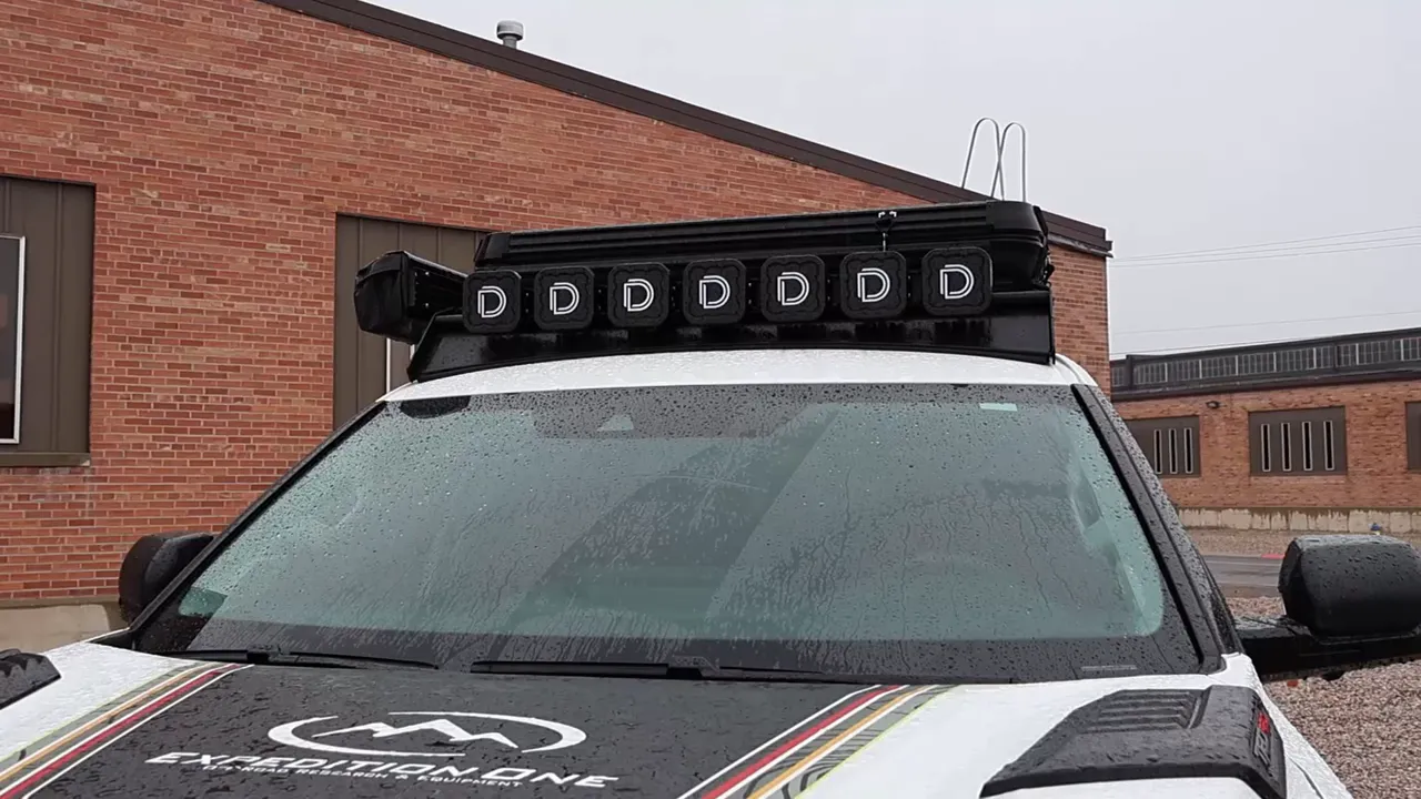 Expedition One roof rack with multi‑pod LED lights mounted above a white Toyota Sequoia windshield in the rain