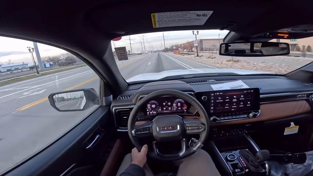 Clear driver point-of-view interior photo of 2026 GMC Canyon showing steering wheel, digital instrument cluster and infotainment screen with minimal hand obstruction