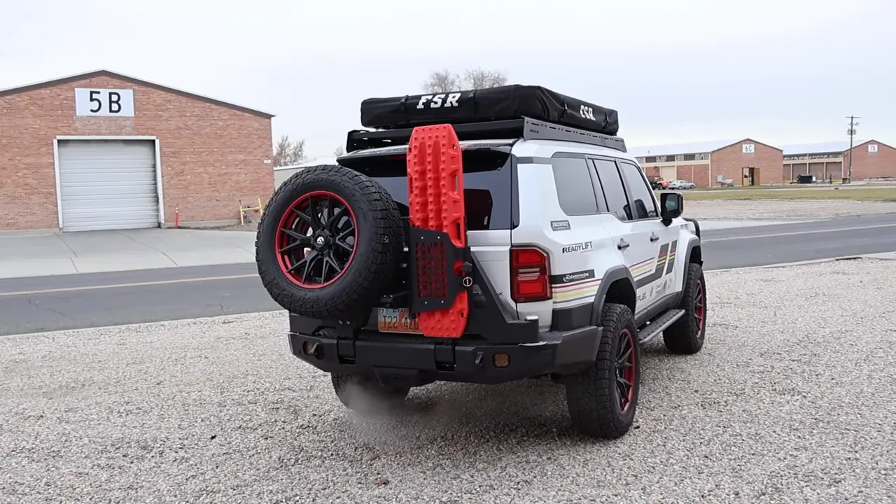 Rear view of Expedition One Land Cruiser with angled spare tire and red traction board mounted to swing gate