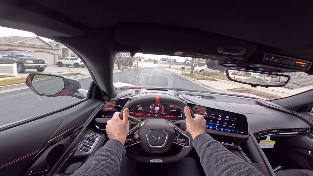 Centered driver point-of-view in a 2026 Corvette Z06 showing both hands at 9 and 3 on the steering wheel and the digital tachometer at 26.