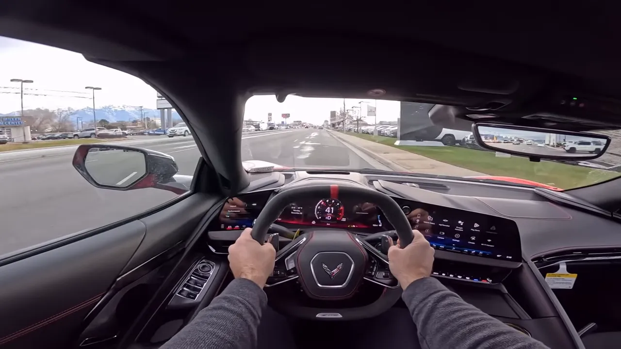 Centered driver point-of-view showing the Corvette Z06 steering wheel, prominent digital tachometer and hands at 9 and 3 while driving.