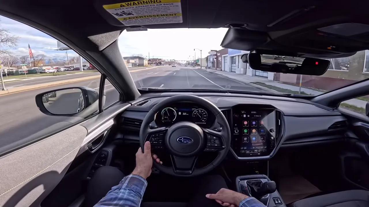Driver point-of-view interior shot of a Subaru showing the steering wheel with Subaru badge, digital instrument cluster, center touchscreen and the road ahead (wide, well-lit).