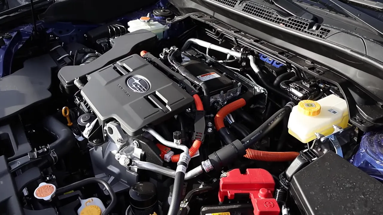 Angled clear view of Subaru 2.5L hybrid engine bay with Subaru logo, orange high-voltage cables and fluid reservoirs