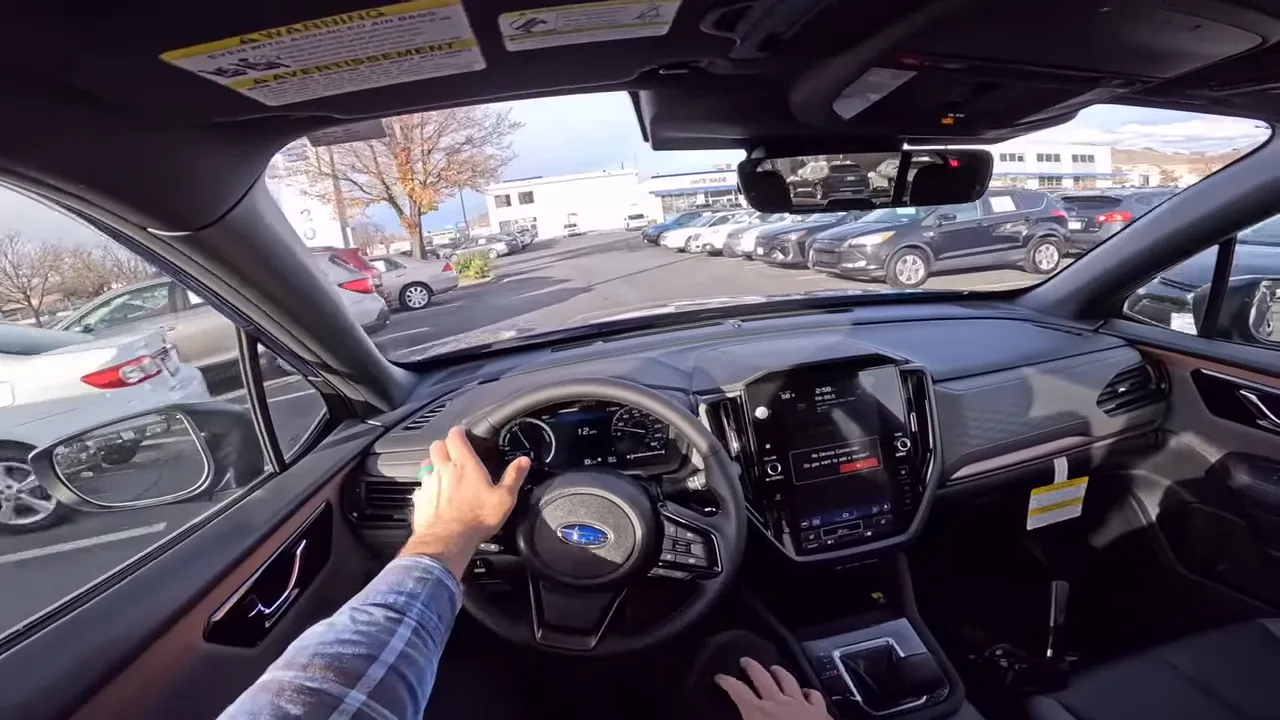 Subaru driver POV showing steering wheel with Subaru badge, instrument gauges, center touchscreen and road ahead