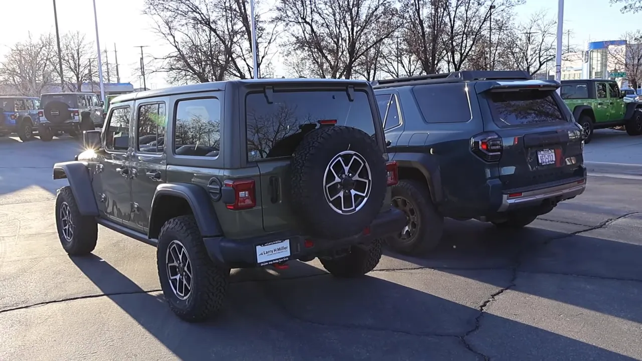 Wide rear view of a Jeep Wrangler with spare on the swing-out tailgate parked beside a Toyota 4Runner Trailhunter, highlighting tailgate and cargo-area packaging